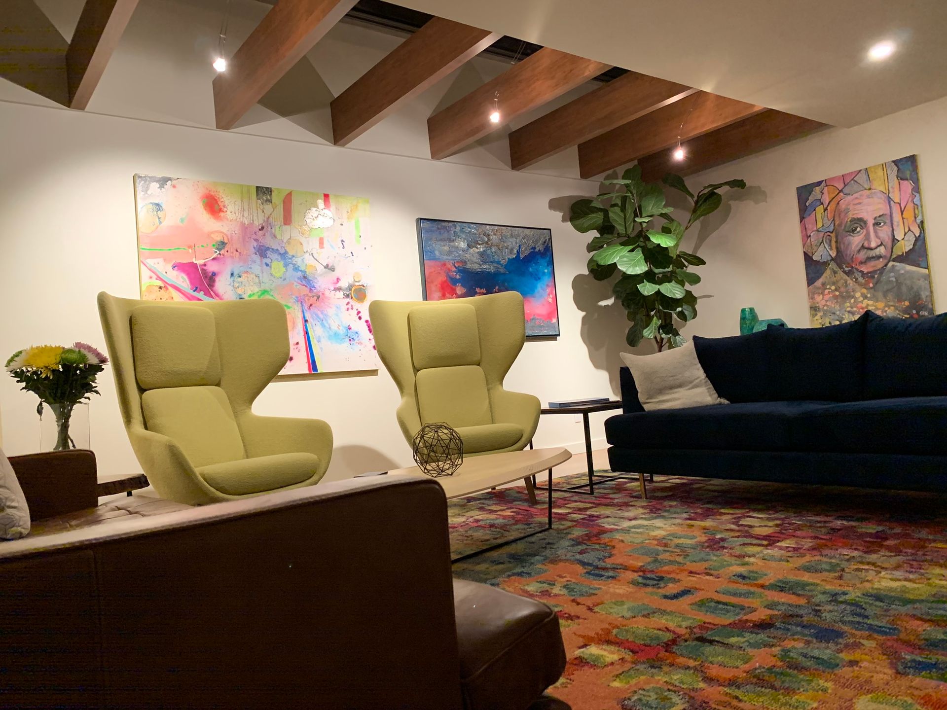Living room with two green armchairs, blue sofa, colorful rug, and abstract art.