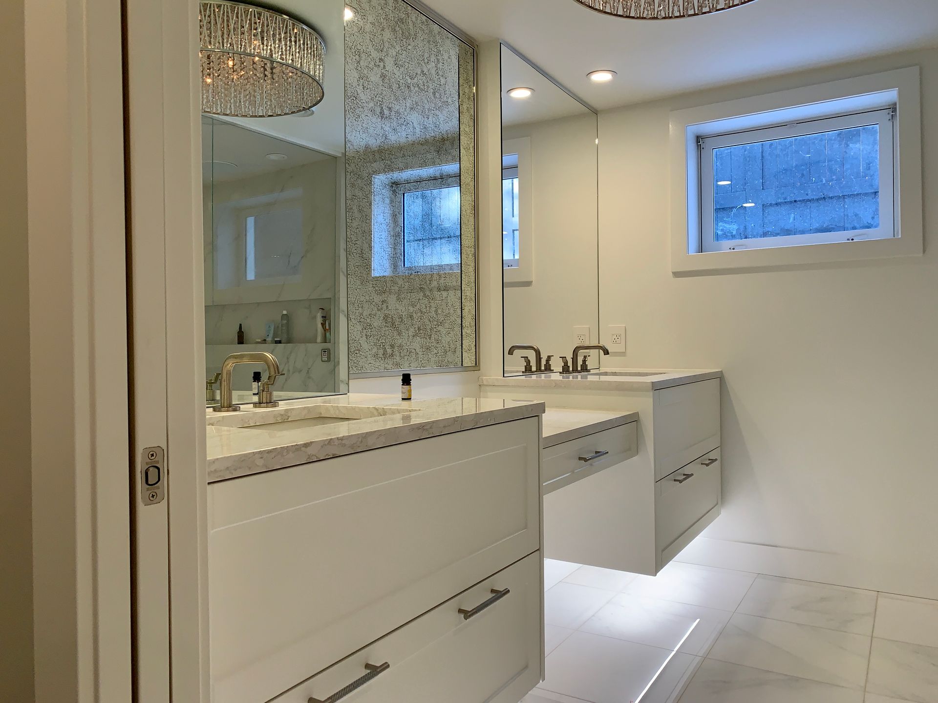 Bright white modern bathroom with double vanity, large mirrors, and decorative lighting.