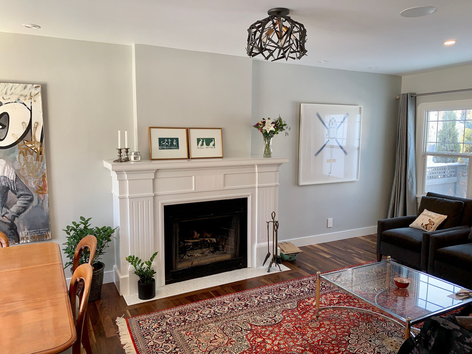 Living room with a white fireplace, floral bouquet, artwork, rug, and dark gray furniture.