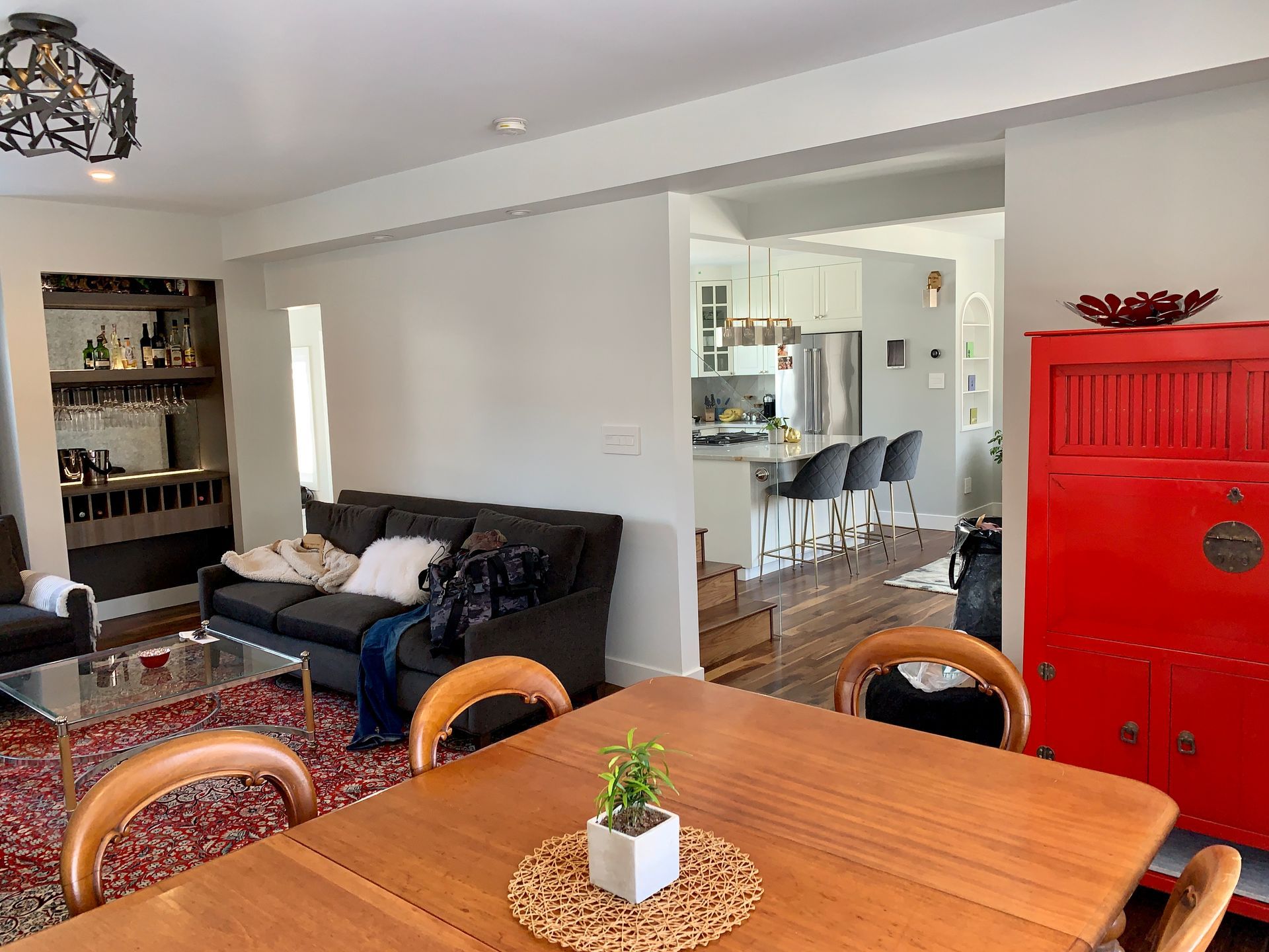 Living room with dining area, gray walls, dark sofa, red cabinet, and view into kitchen with bar stools.