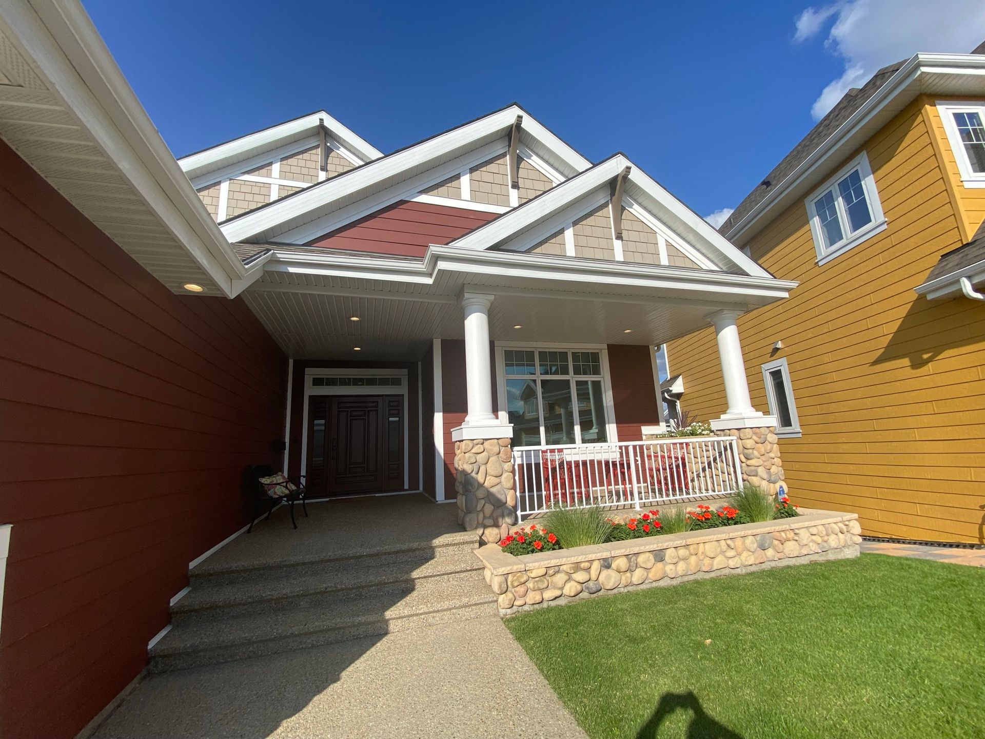 Red and beige house with porch, stone facade, and green lawn on a sunny day.