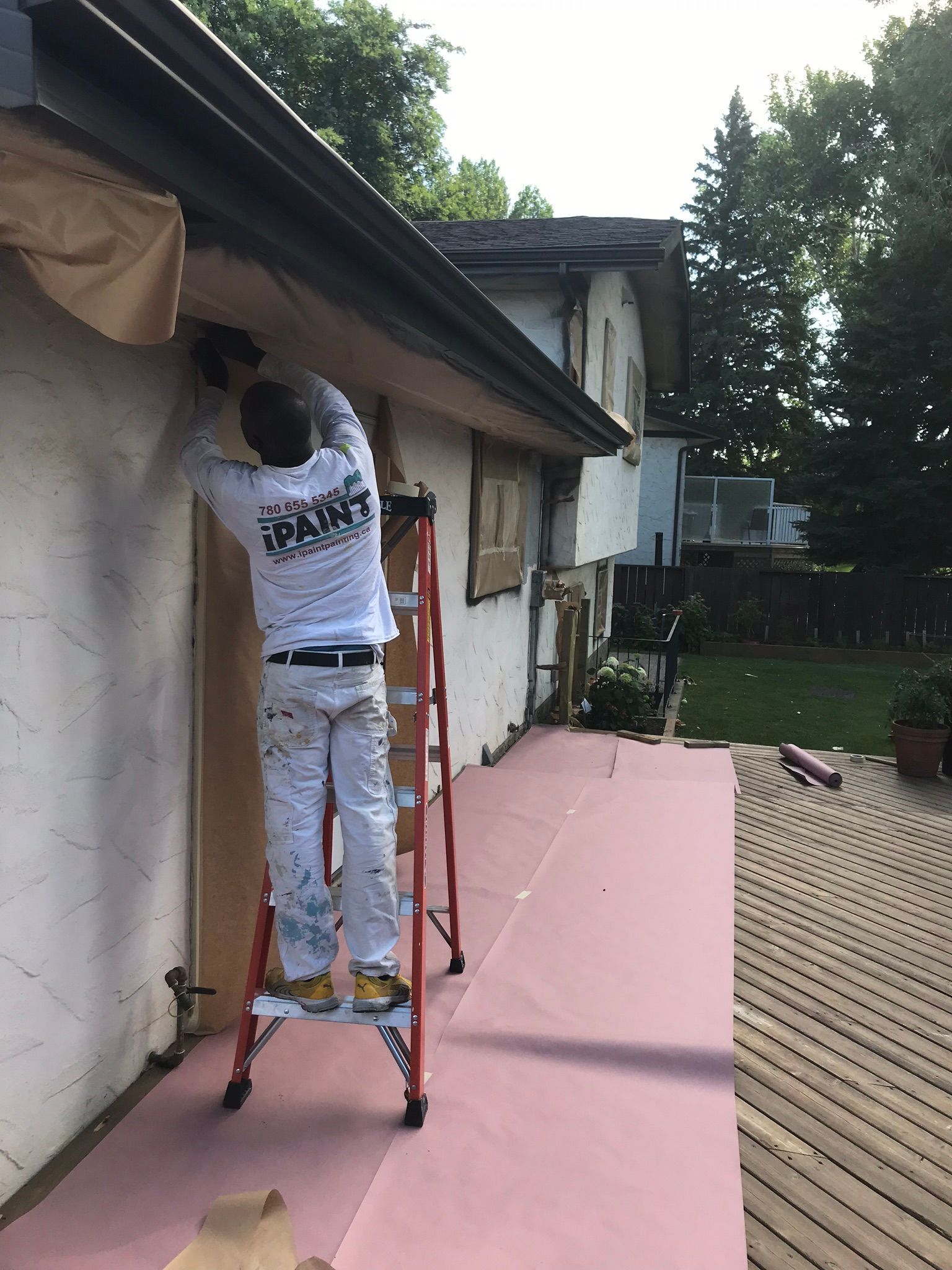 A man is standing on a ladder painting the side of a house.