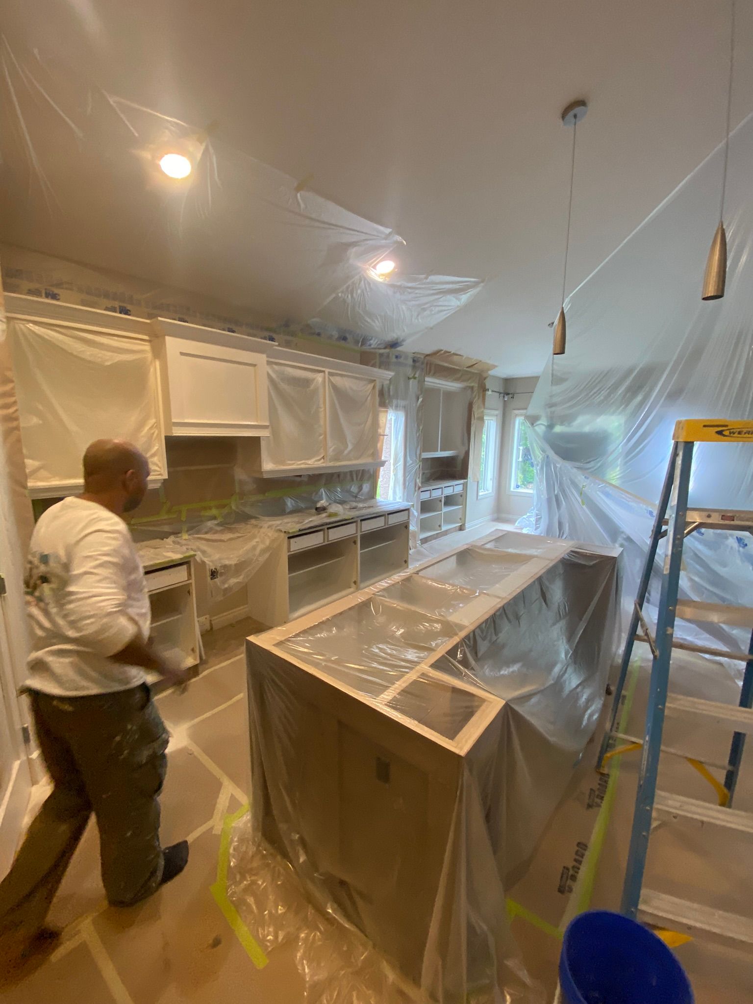A man is standing in a kitchen covered in plastic.