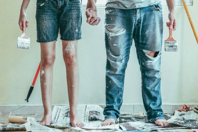 A man and a woman are standing next to each other holding paint brushes.