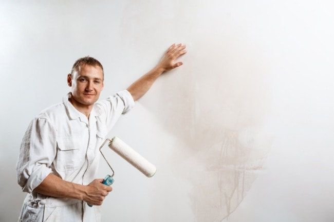 A man is painting a wall with a paint roller.