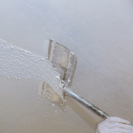 A person is scraping a ceiling with a scraper.