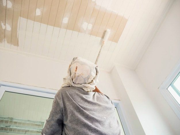 A man is painting a ceiling with a paint roller.