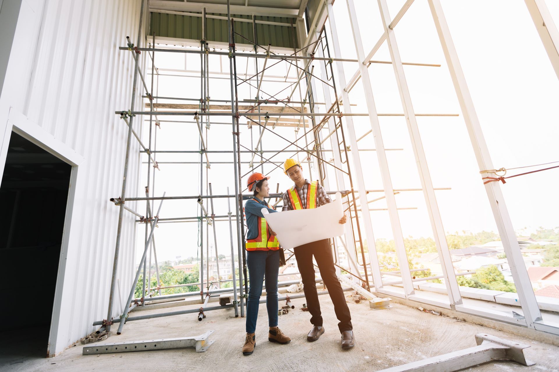 Two construction workers reviewing blueprints on a partially constructed building