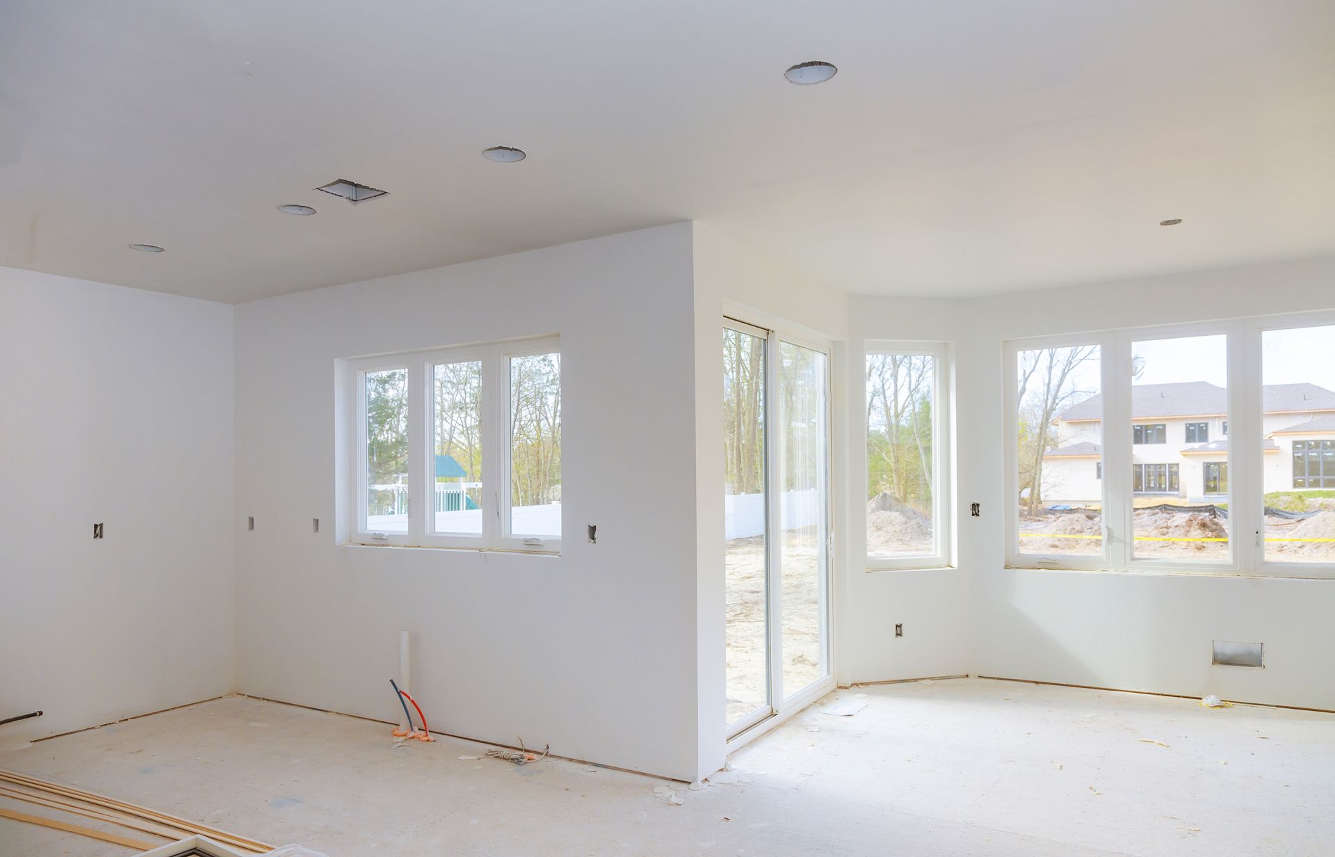 Empty white-walled room with windows. Construction in progress, unfinished floor