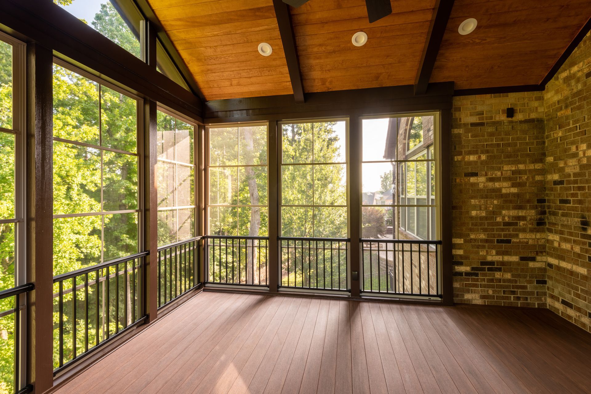 Sunroom with large windows, wood ceiling, brick wall, and brown flooring overlooking trees