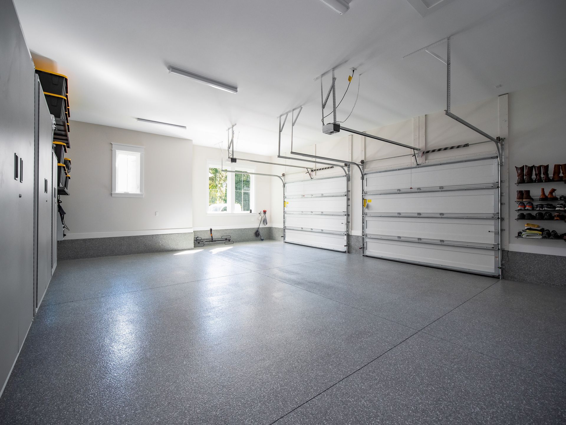 Empty, clean garage with light gray speckled flooring, white walls, and two garage doors.