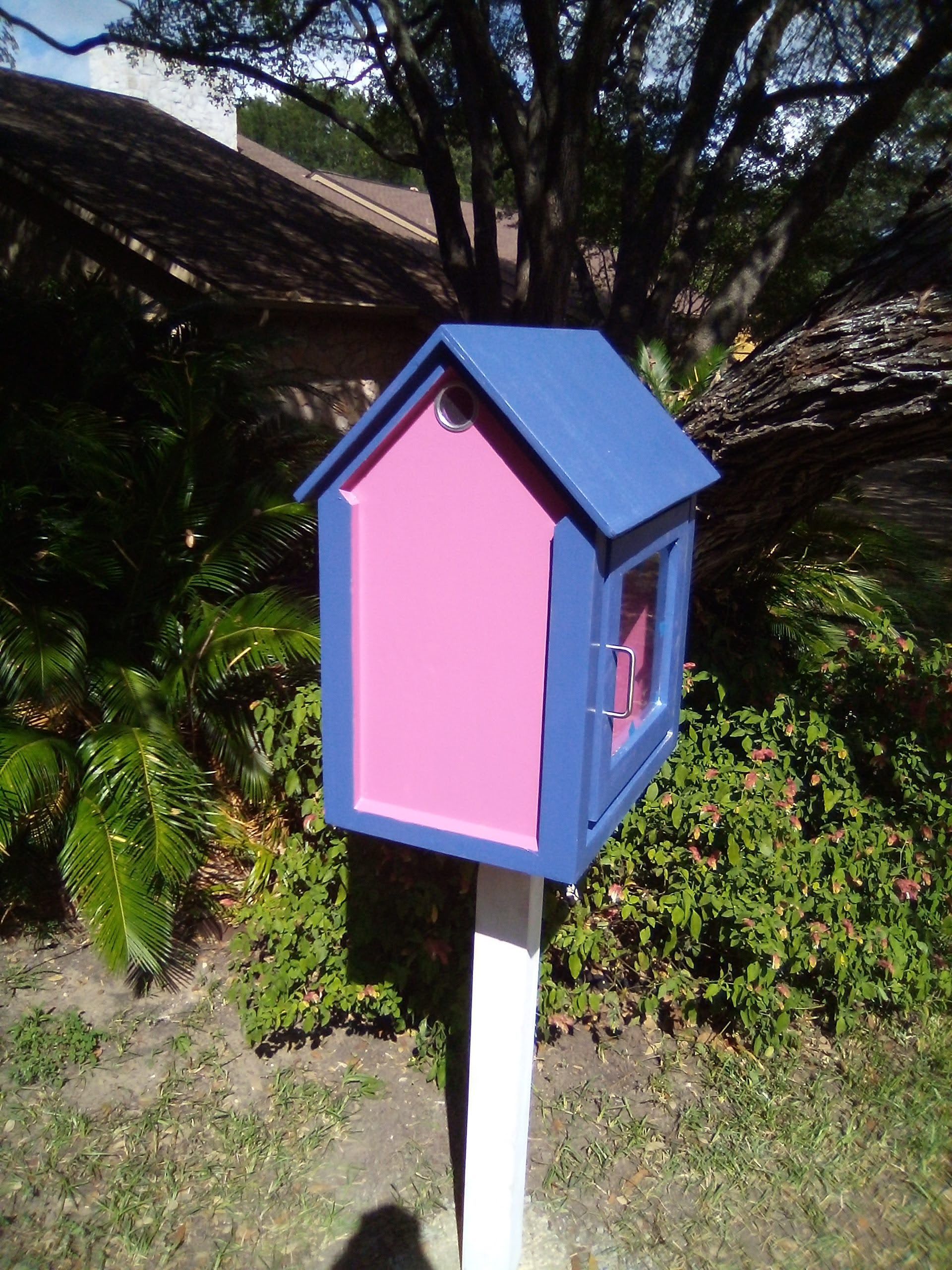 A small blue and pink house on a white pole