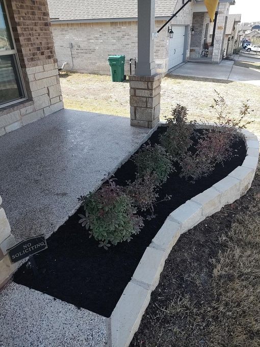 A planter with plants and mulch in front of a house.