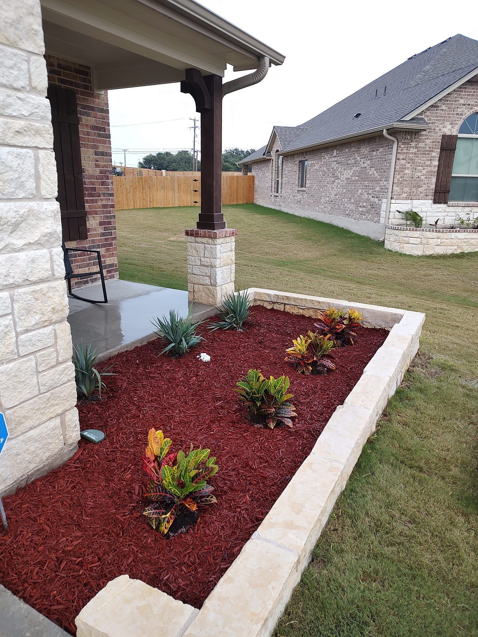 A garden with plants and mulch in front of a brick house.