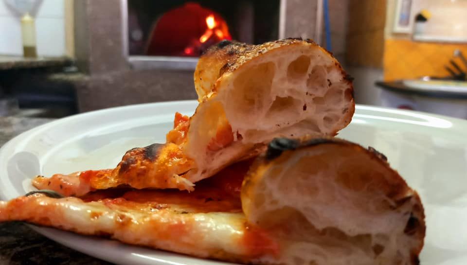 Una fetta di pizza è su un piatto bianco davanti a un forno per pizza.