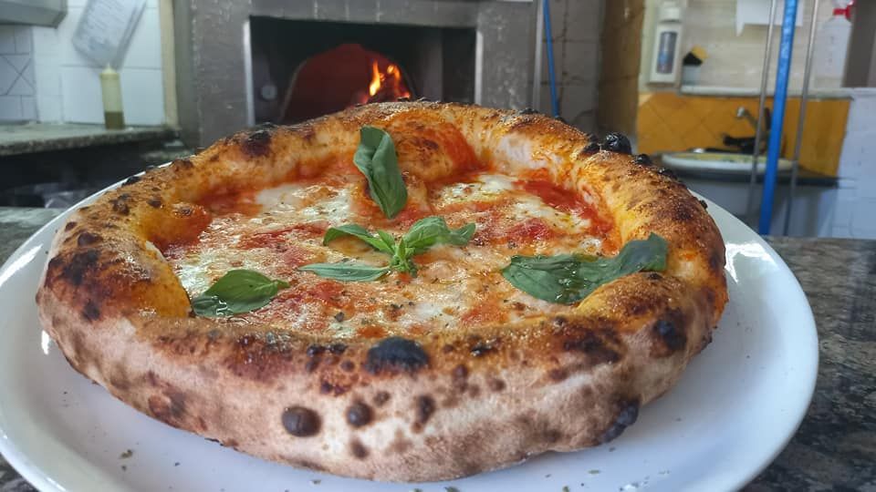Una pizza è appoggiata su un piatto bianco davanti a un forno per pizza.