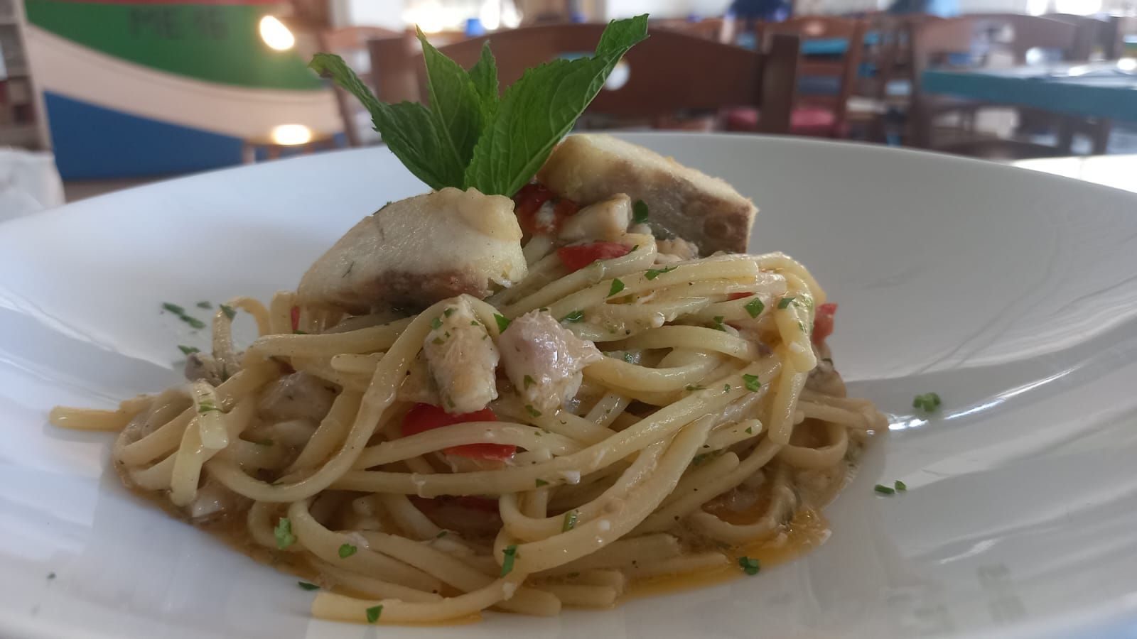 Un primo piano di un piatto di pasta con un pezzo di pesce sopra.