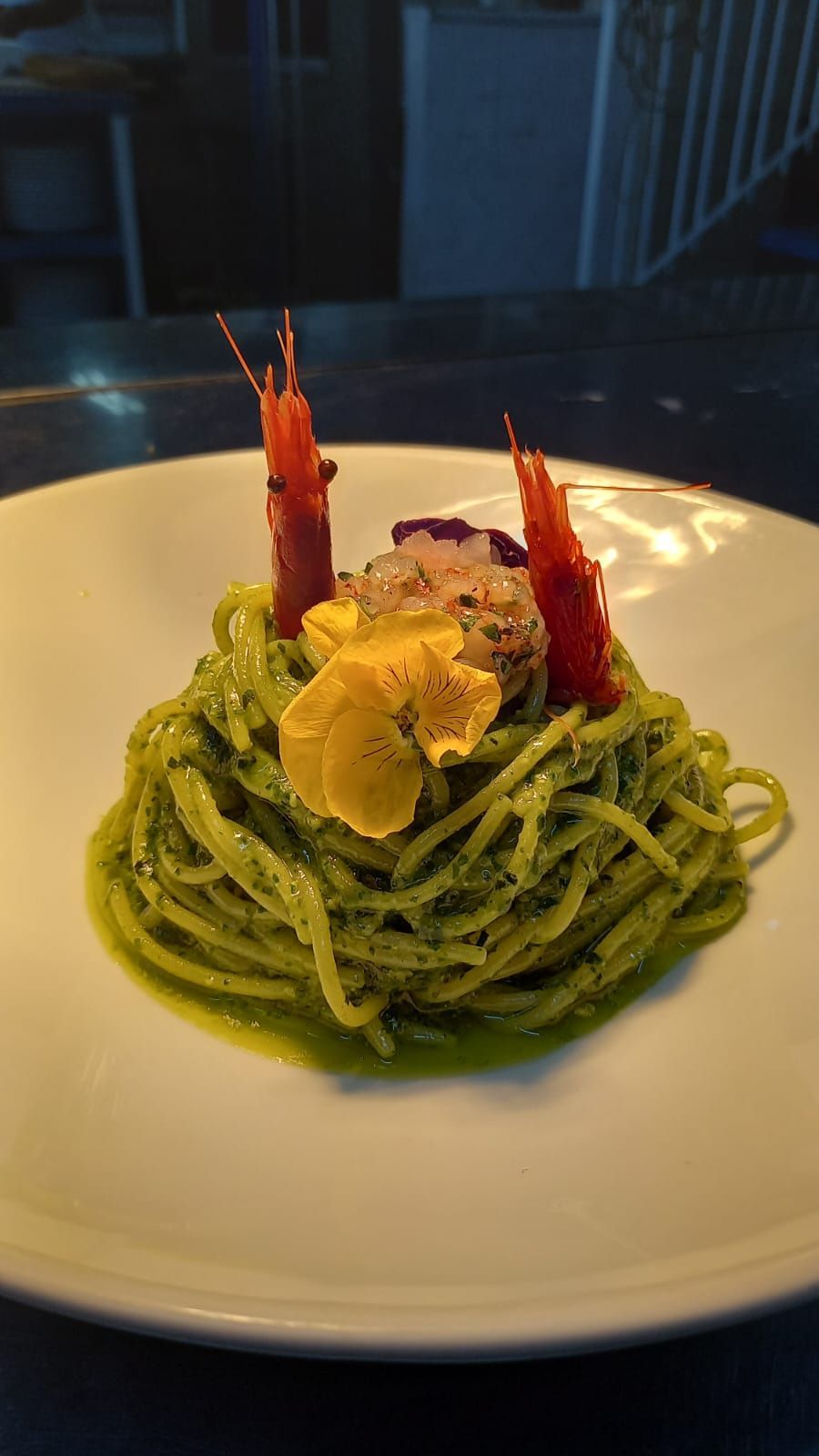 Un piatto bianco con sopra tagliatelle e gamberetti su un tavolo.