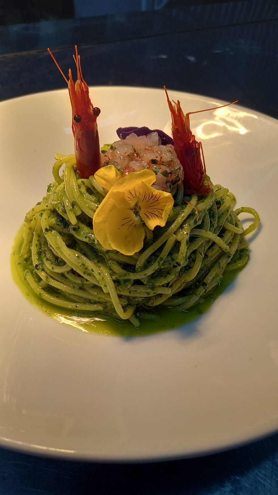 Un piatto bianco con sopra spaghetti e gamberi su un tavolo.