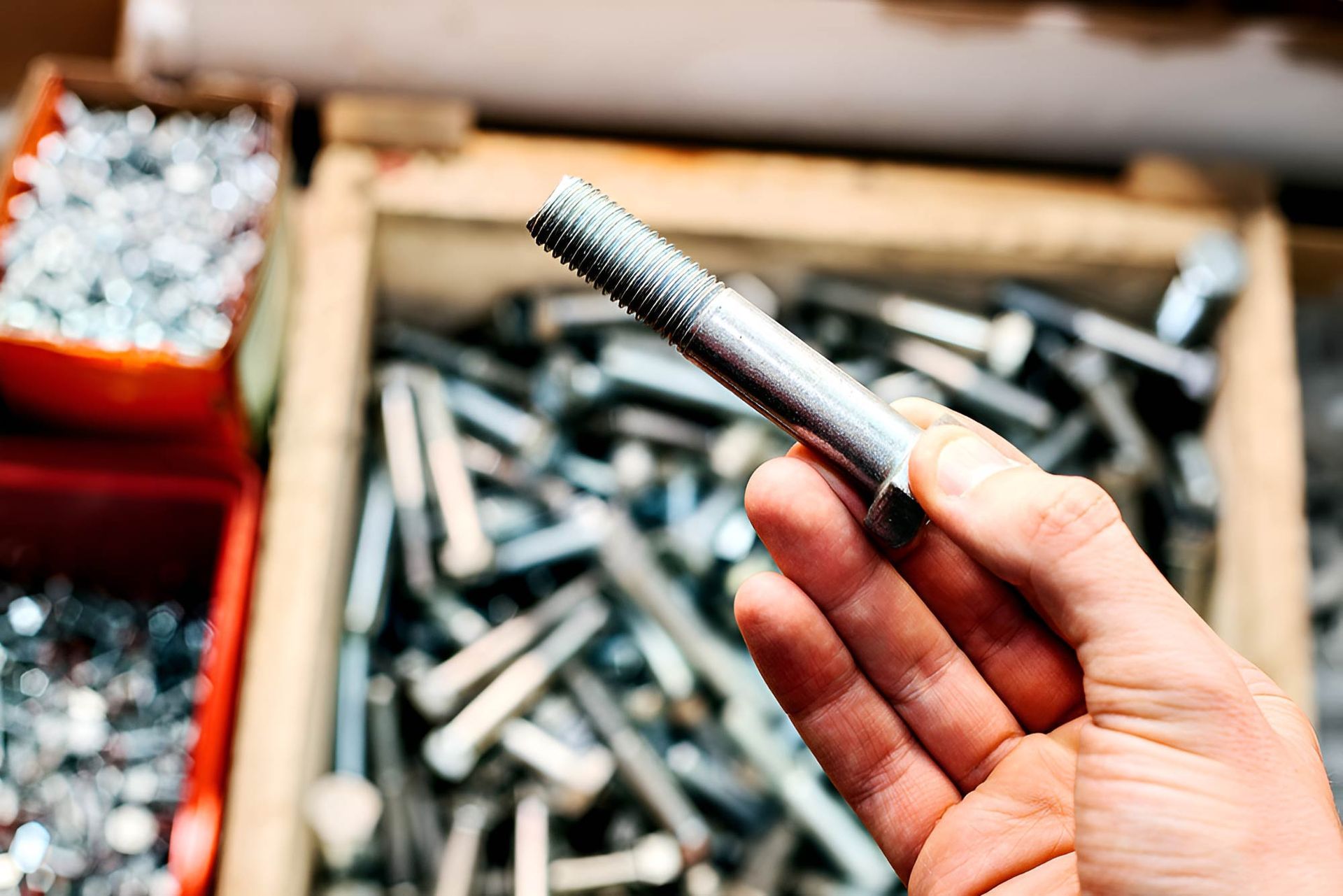 A Person Is Holding A Bolt In Their Hand In Front Of A Box Of Bolts — Wallers Precision Tooling In Paget , QLD