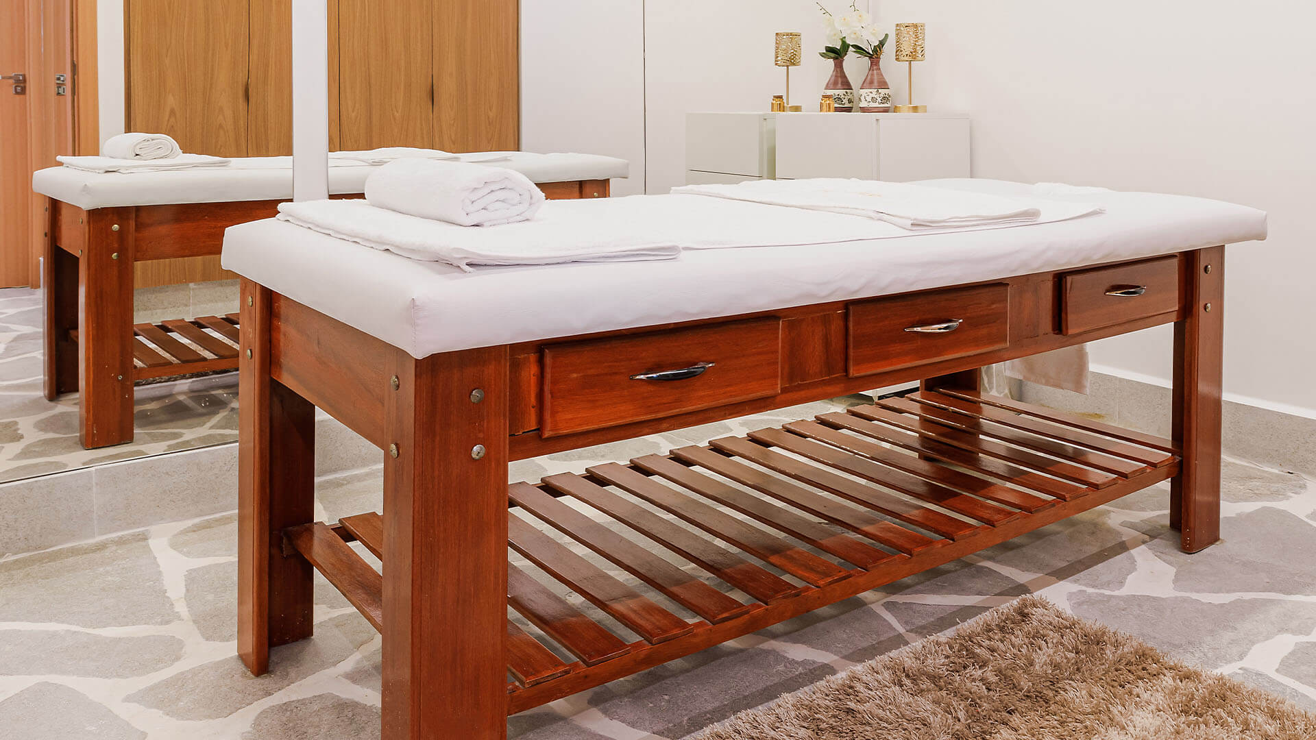 Duas mesas de massagem de madeira em uma sala com toalhas sobre elas.