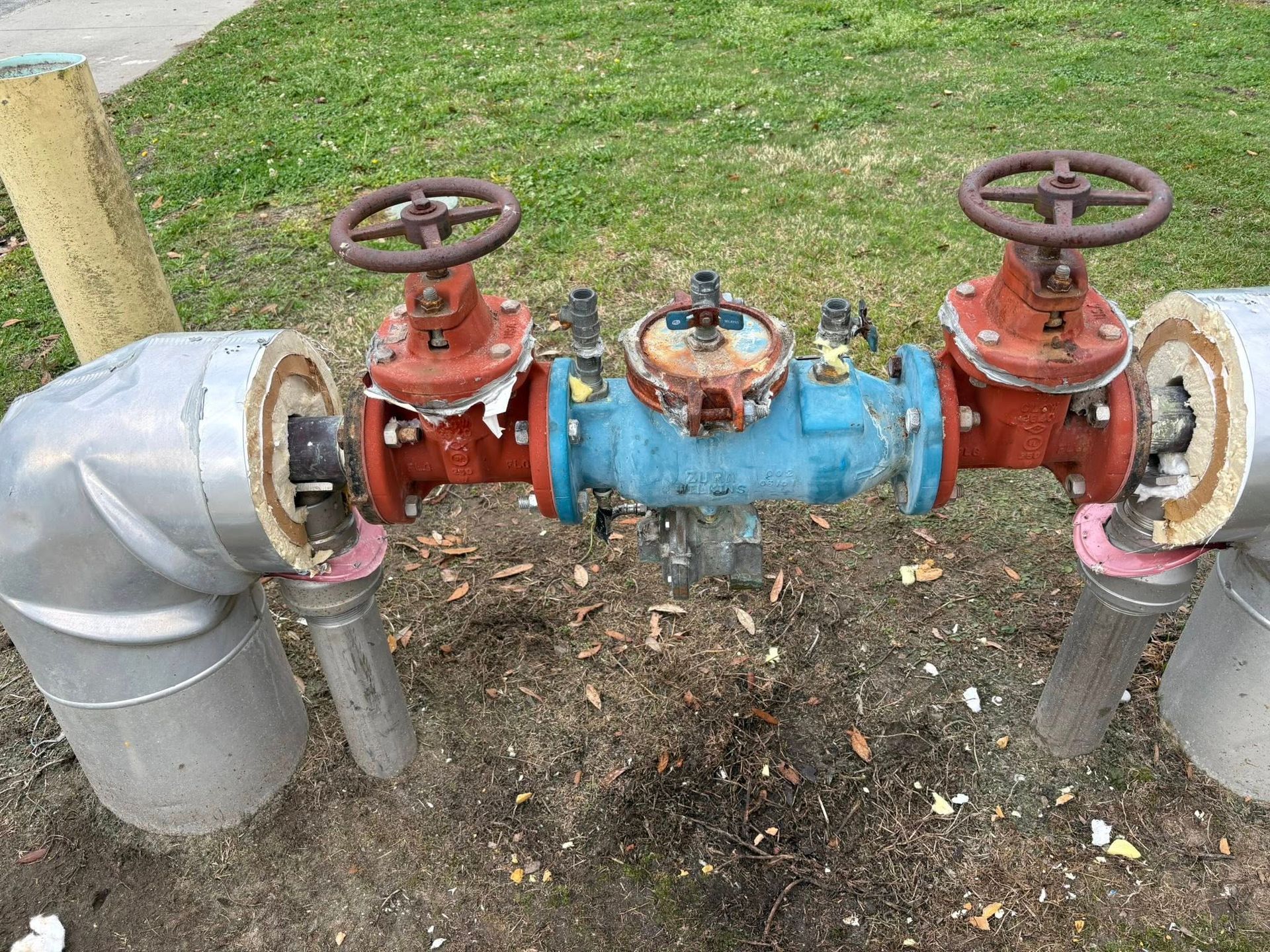 Red and blue outdoor pipeline valves with wheel handles on a grassy utility line