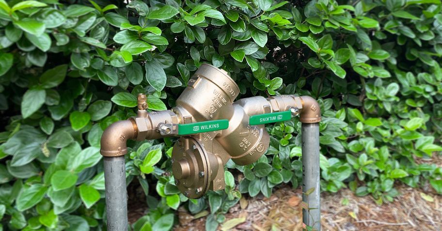Outdoor brass water meter and pipes in front of green hedges
