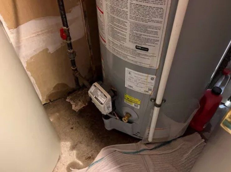 Water heater in a utility closet with wet floor and a leak detector near the base.