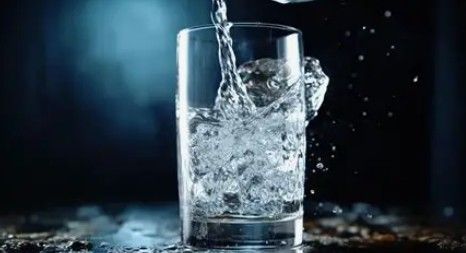 Water pouring into a clear glass, splashing on a dark surface.