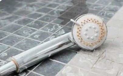 Silver showerhead with water droplets lying on a tiled floor