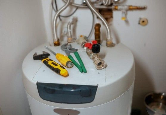 Tools resting on top of a white water heater in a small utility room.