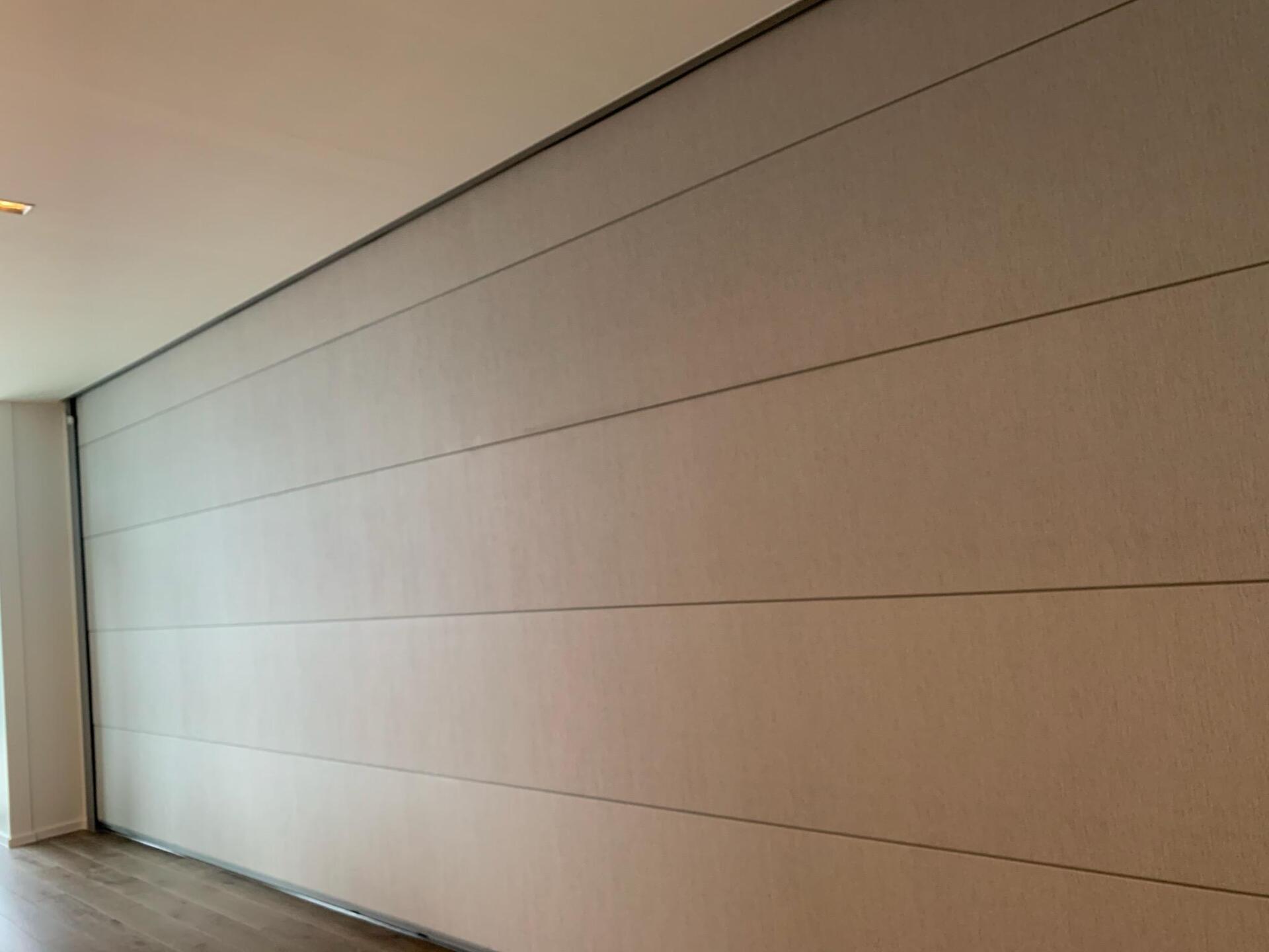 A wall with horizontal panels, light color, next to a door frame. Ceiling is white, floor is wood.