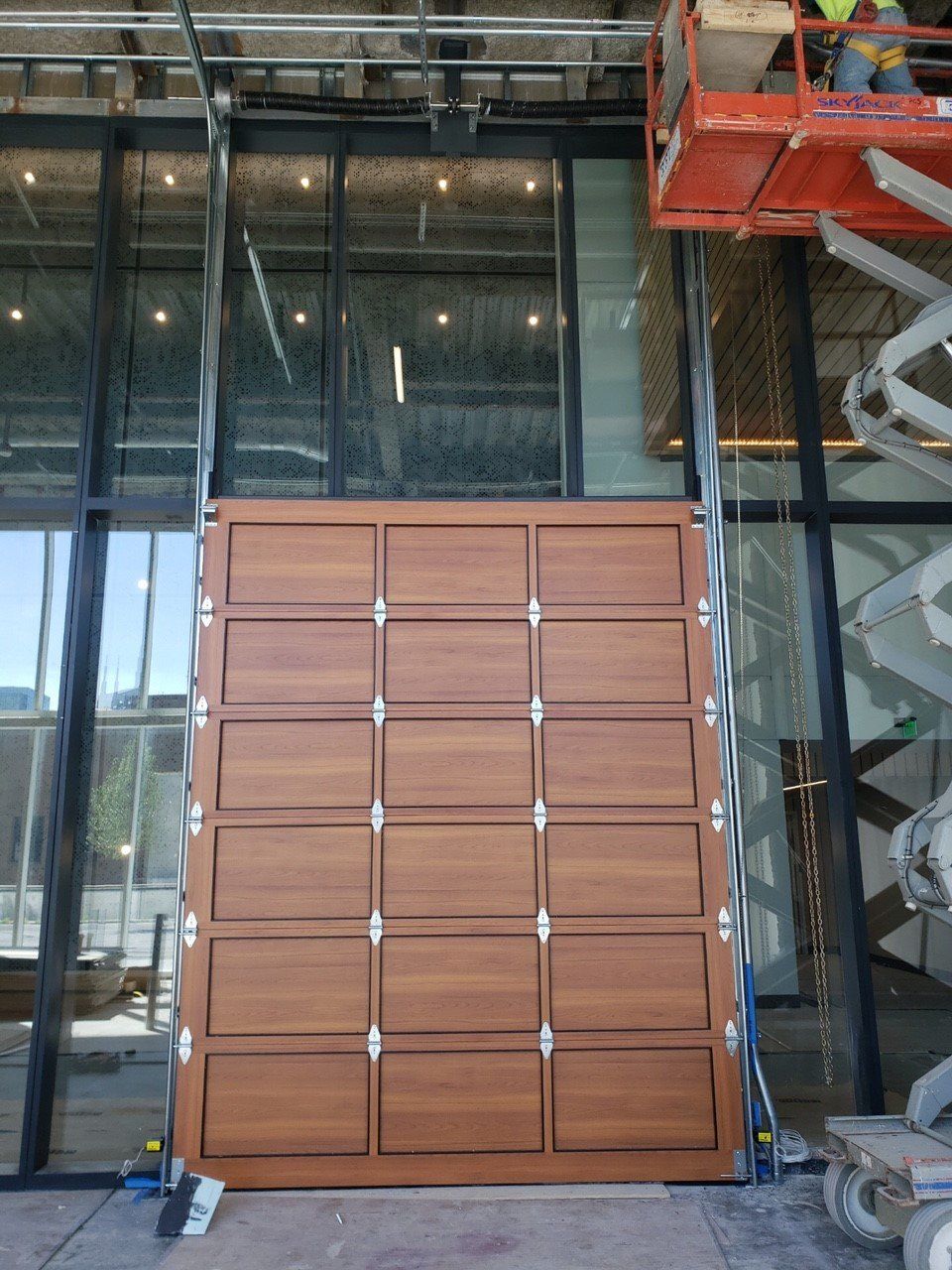 Large wooden wall panel section with multiple square doors, being installed in a modern building with glass and metal framing.