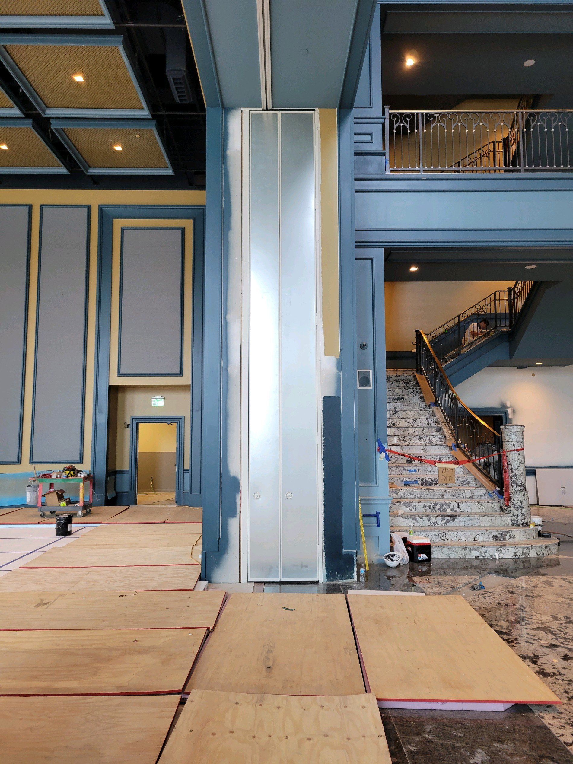 Interior renovation. Column clad in metal. Staircase with black railing, light blue walls, exposed flooring.