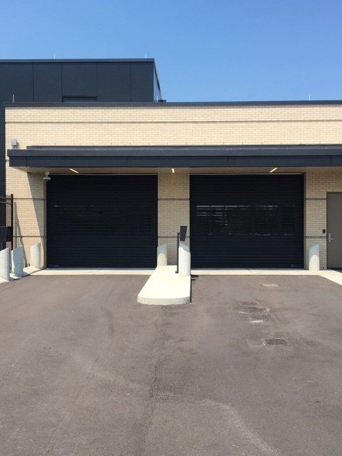Two black garage doors on a light beige building with a small ramp.