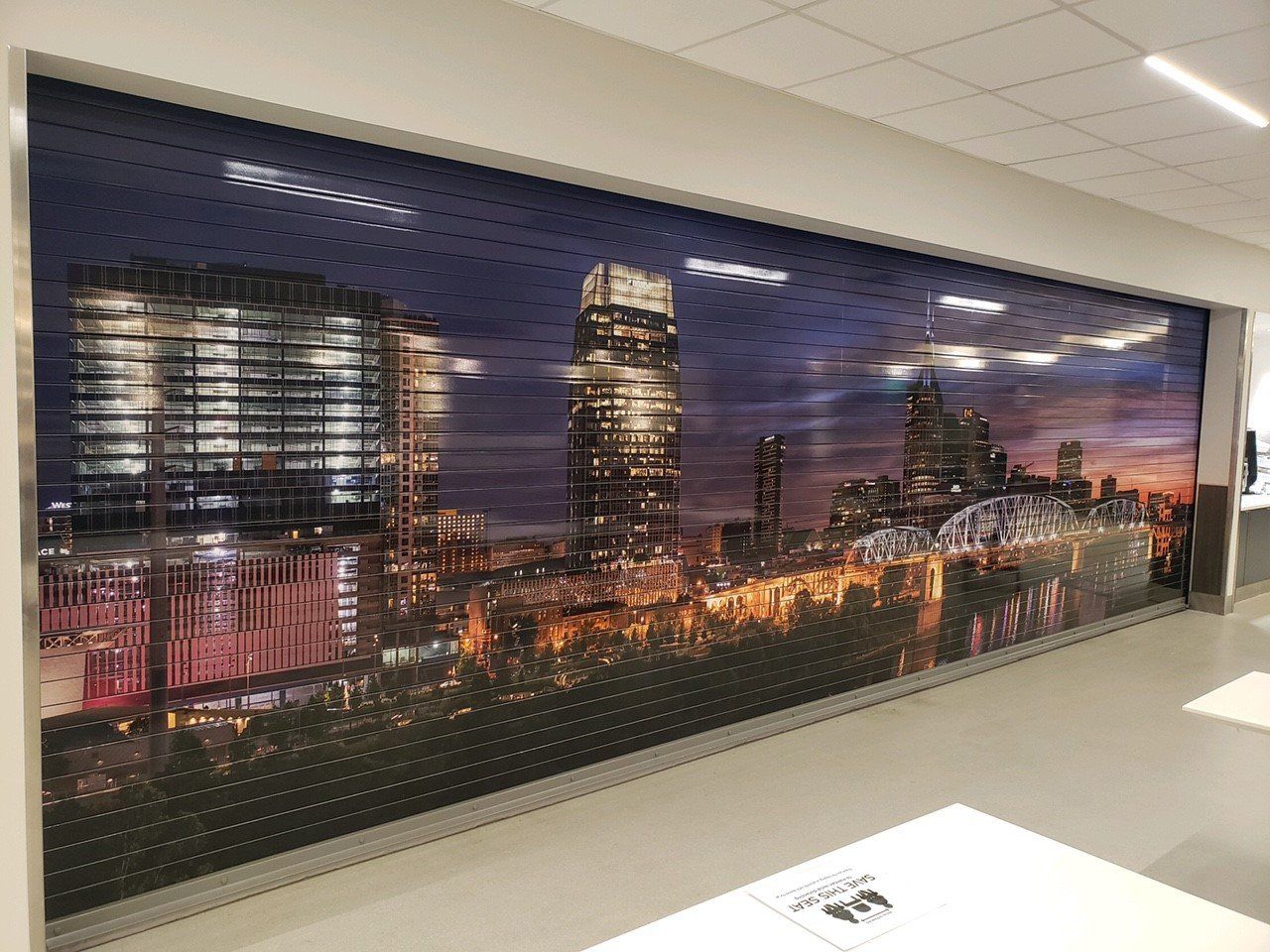 Rolling door with a nighttime cityscape scene. Buildings with lights, dark sky, perforated pattern.