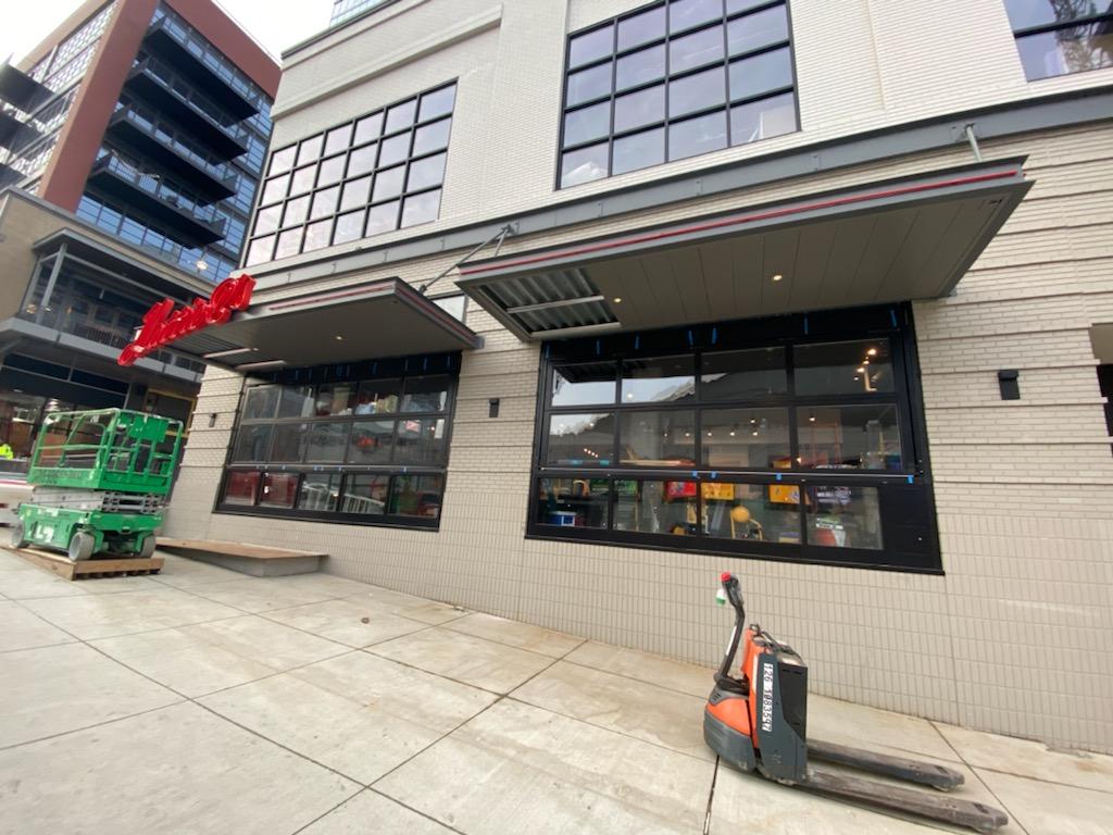 Exterior of a brick building with large glass windows and awnings. A pallet jack sits on the sidewalk.