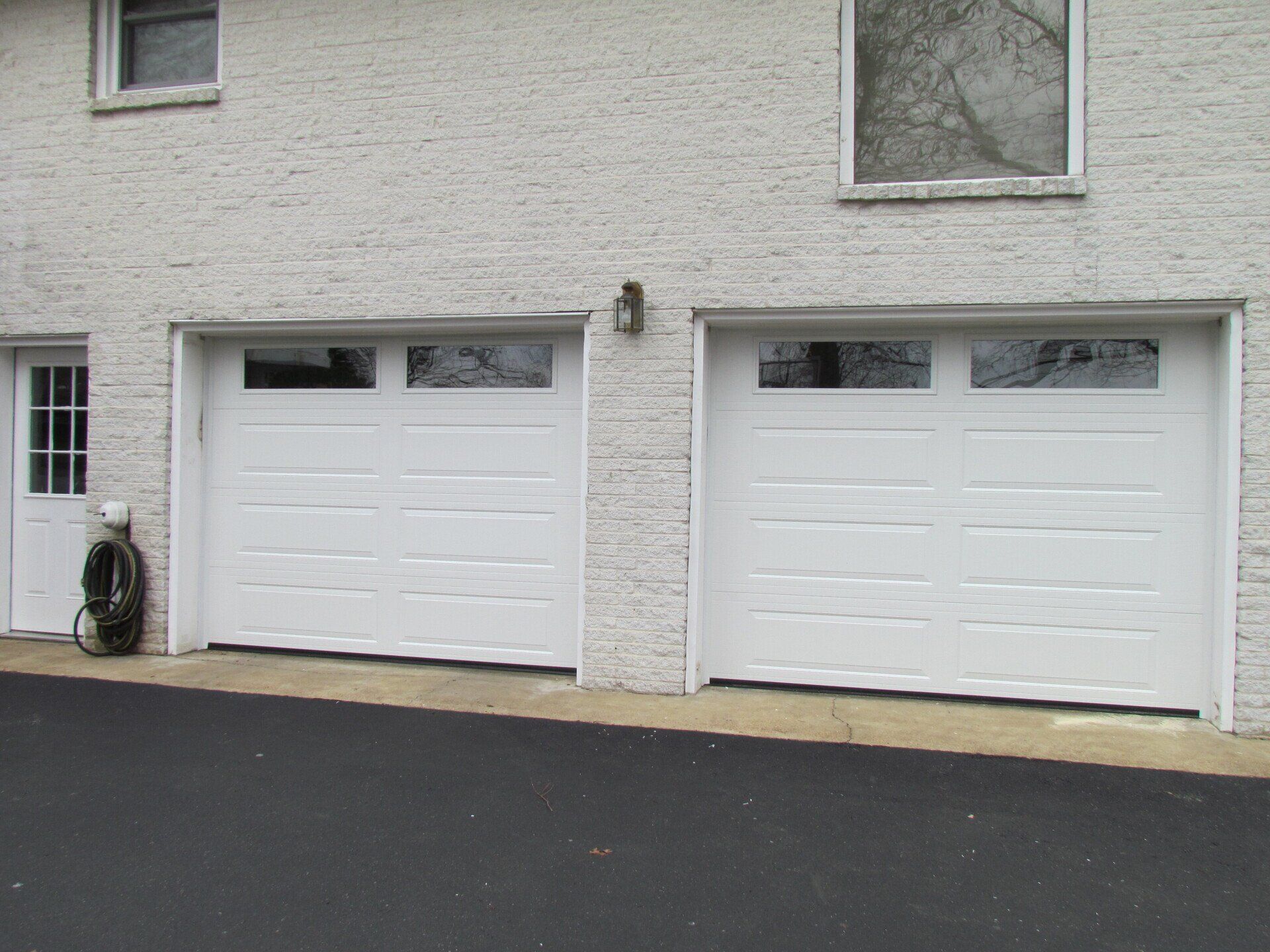 White double garage doors on a light brick building with windows above.