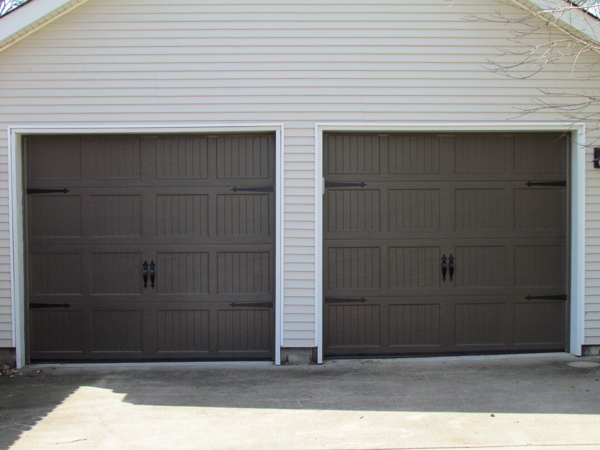 Two brown garage doors on a light-colored house with concrete driveway.