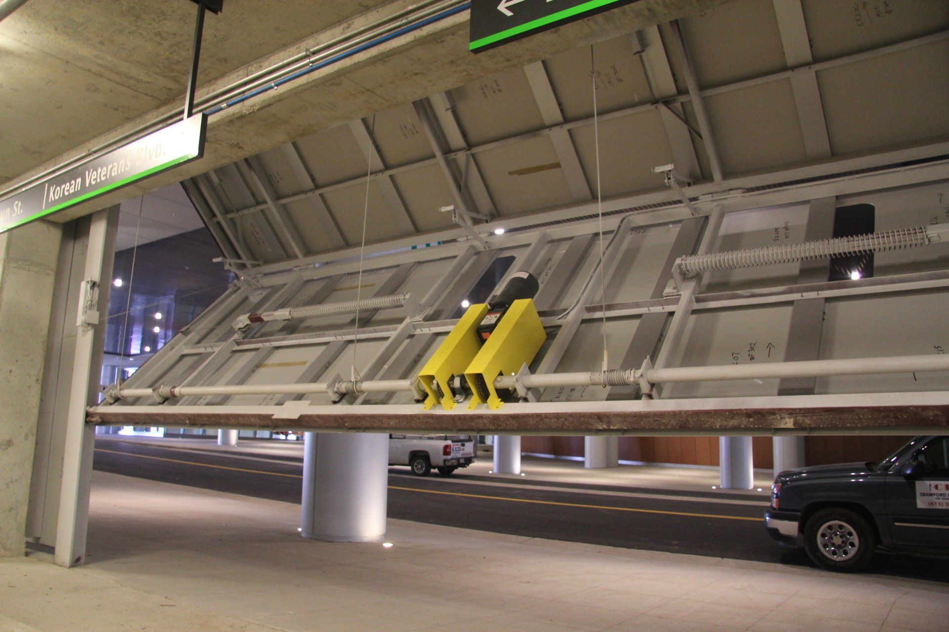 Open, folded overhead door reveals a street with a vehicle and building columns. Yellow lifting mechanisms are visible.