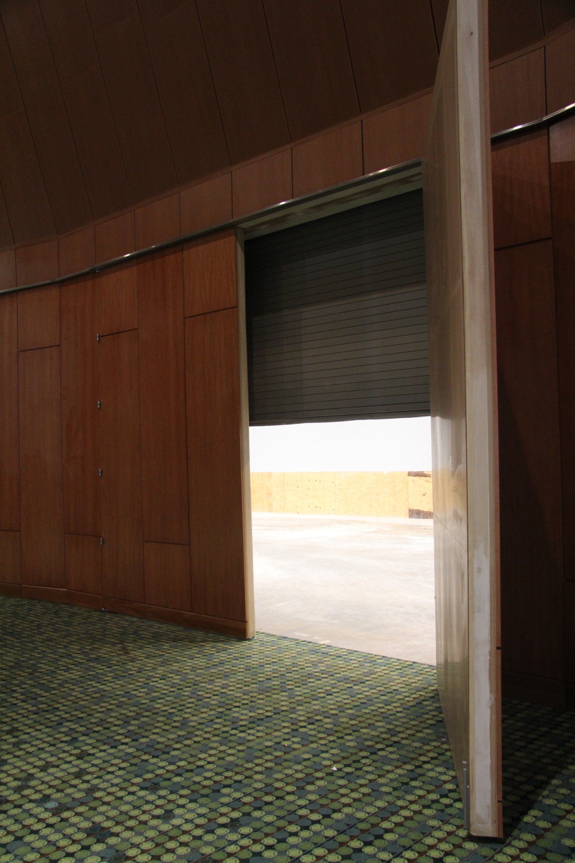 Open wooden door reveals exterior, with a textured roller shade and carpeted interior.