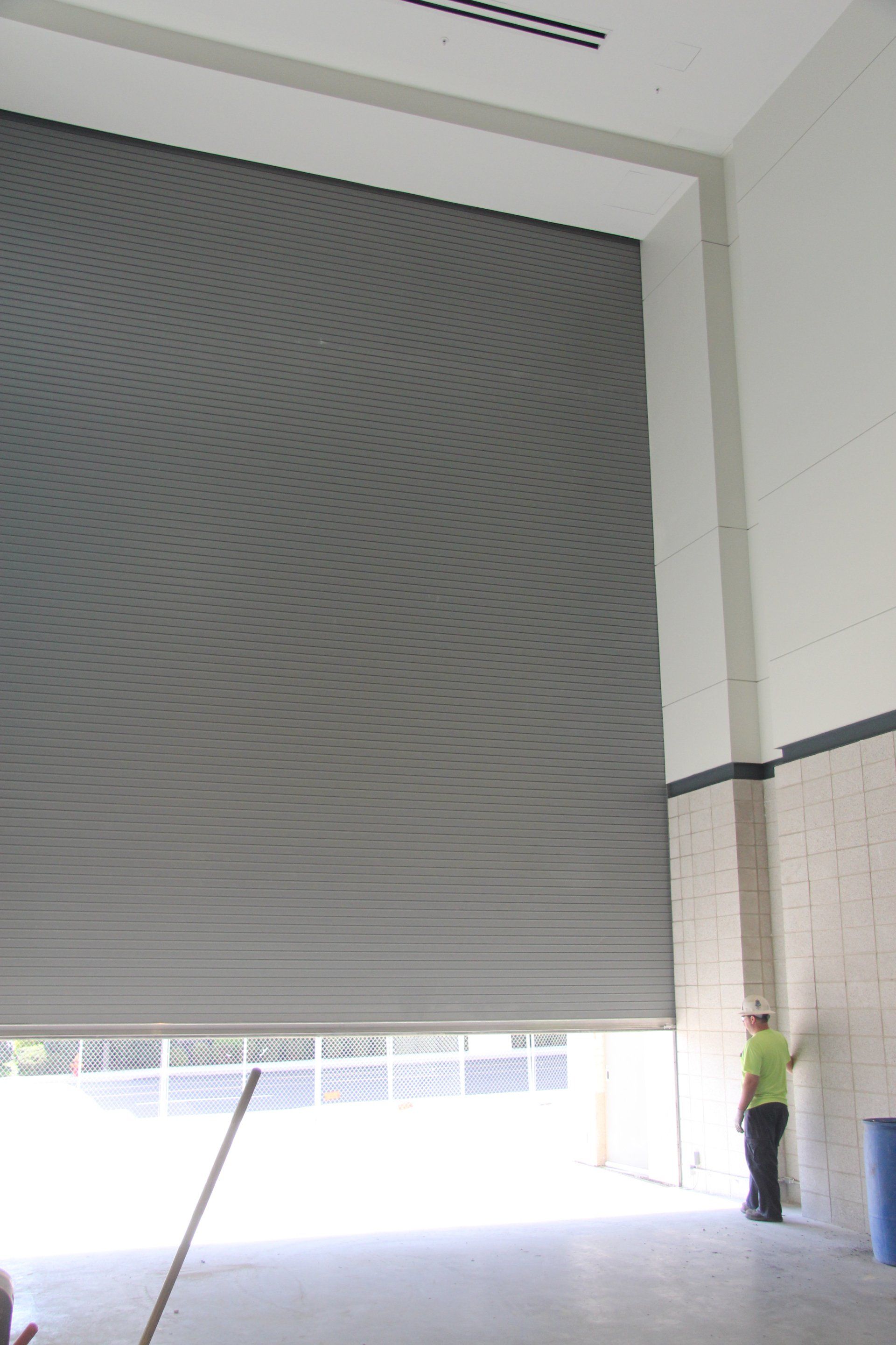Large, partially open gray roll-up door in a building. A person stands near it.