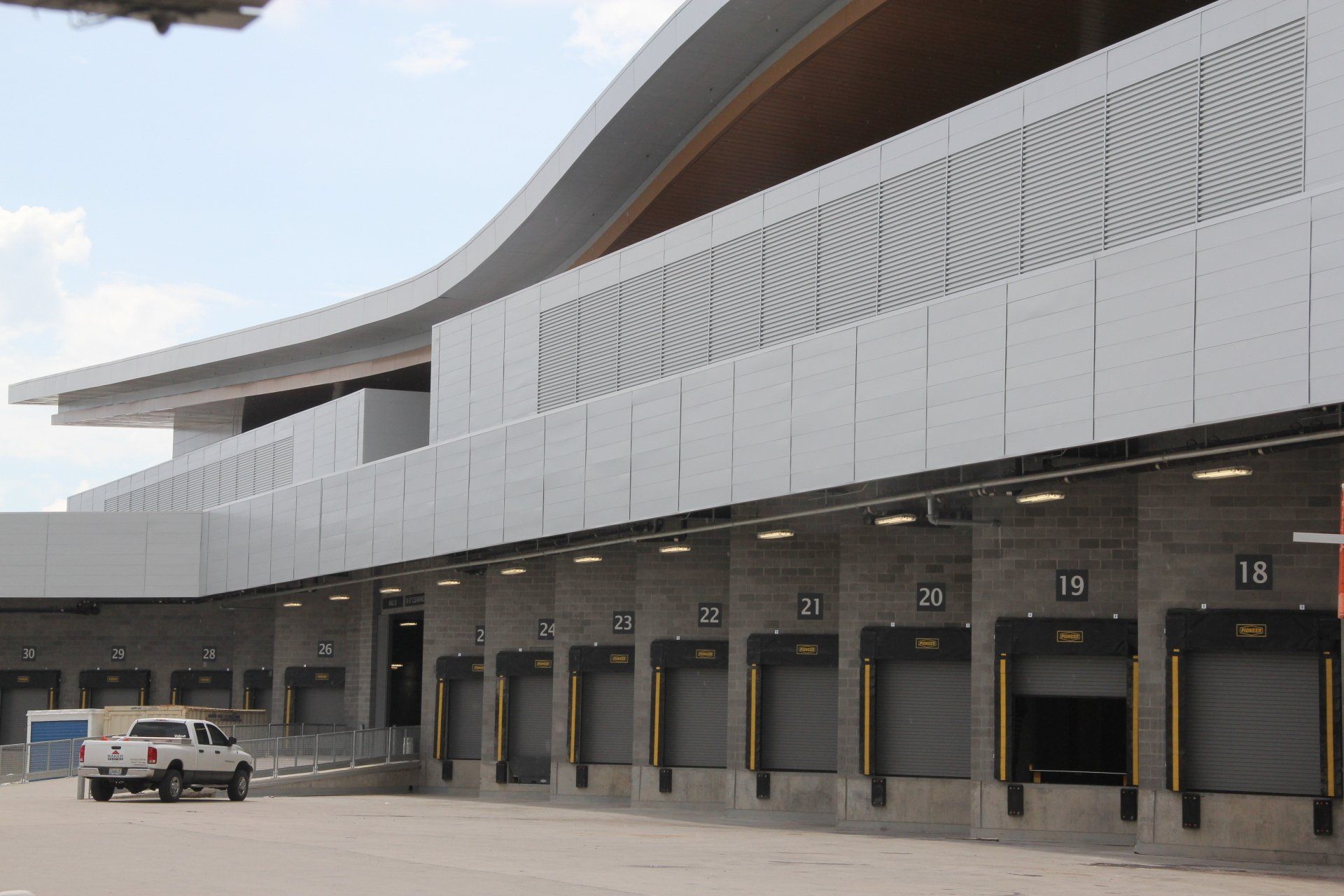 Loading docks with open doors on a modern, gray building; a white pickup truck is parked in front.