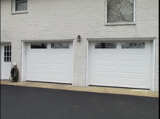 Dual white garage doors with top windows set in a light brick home exterior.