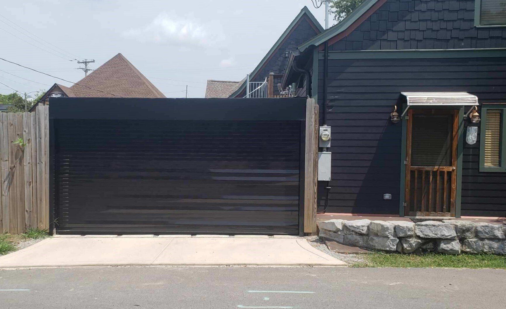 Black garage door next to a dark house with a small porch and stone steps.