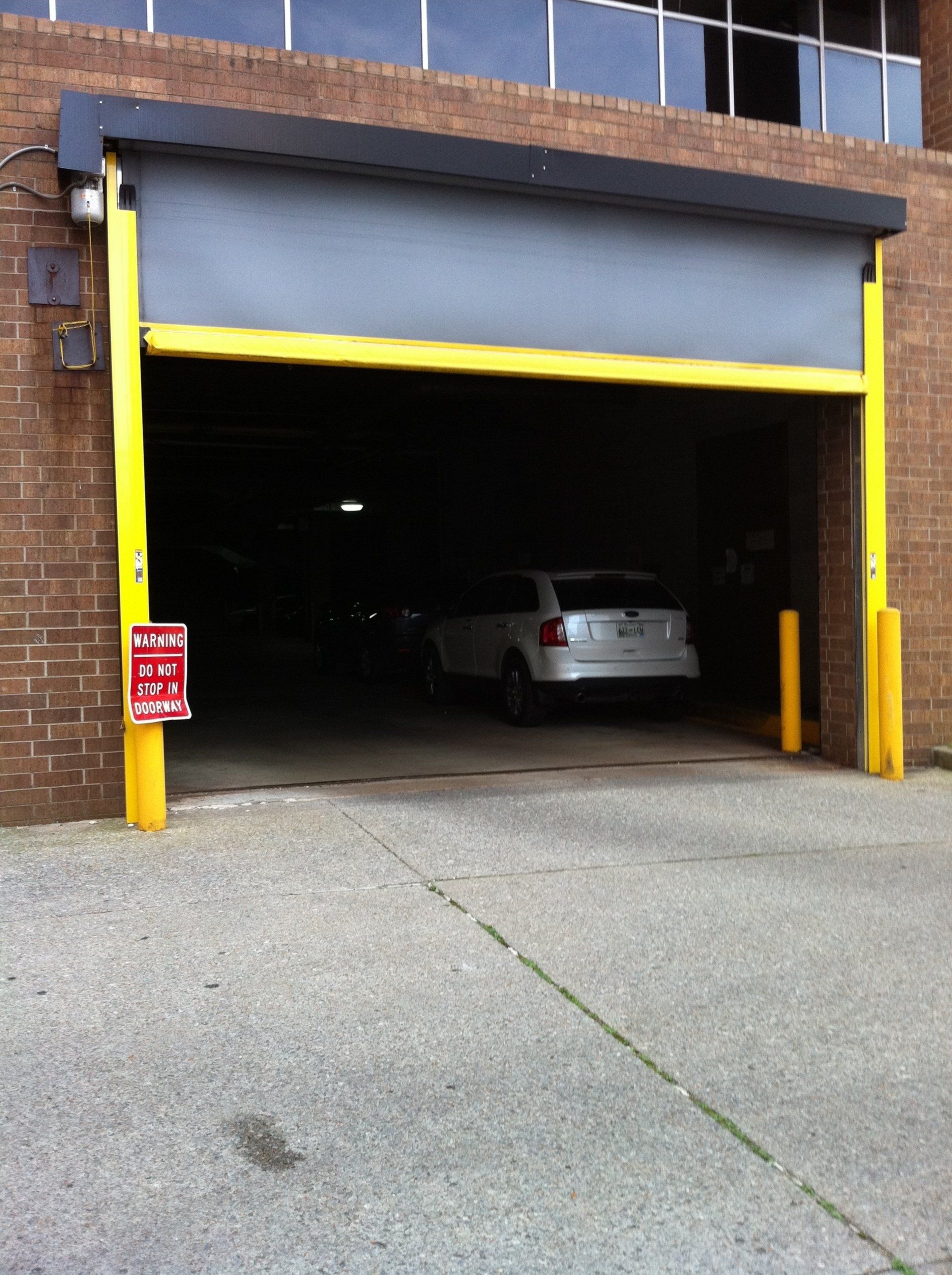 A white car exiting a dark garage. Yellow trim frames the opening, brick building background.