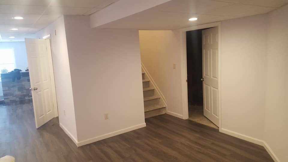 An empty basement with hardwood floors and stairs leading to the second floor.