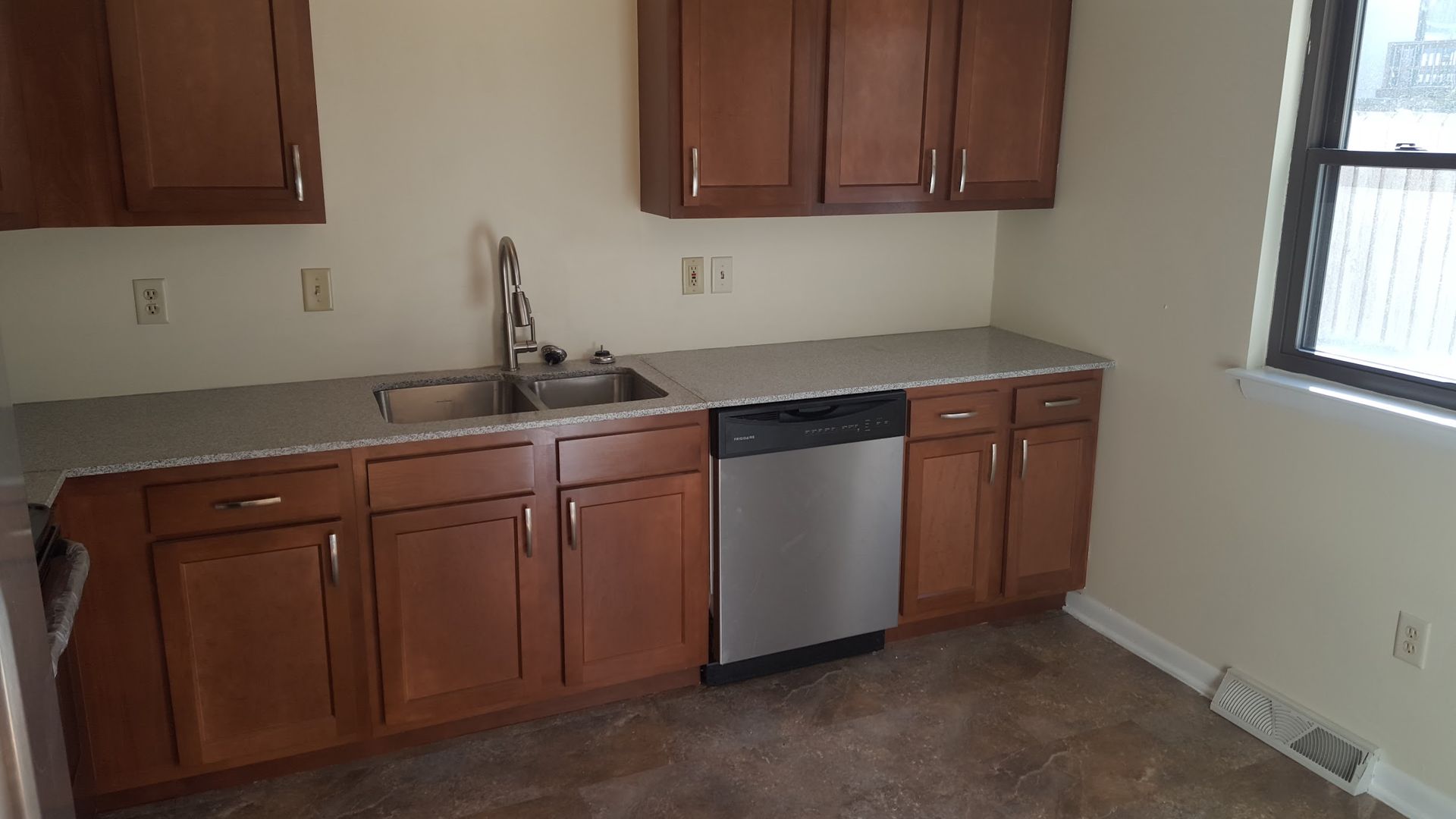 An empty kitchen with wooden cabinets , a sink and a dishwasher.