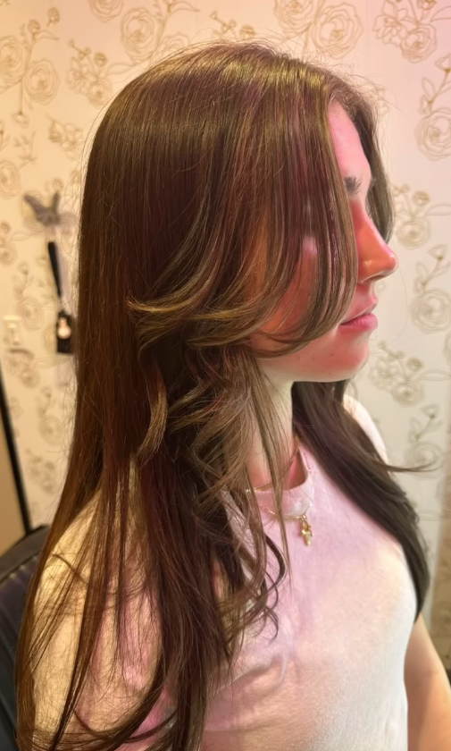 Woman with long, layered brown hair, some lighter strands, side profile.