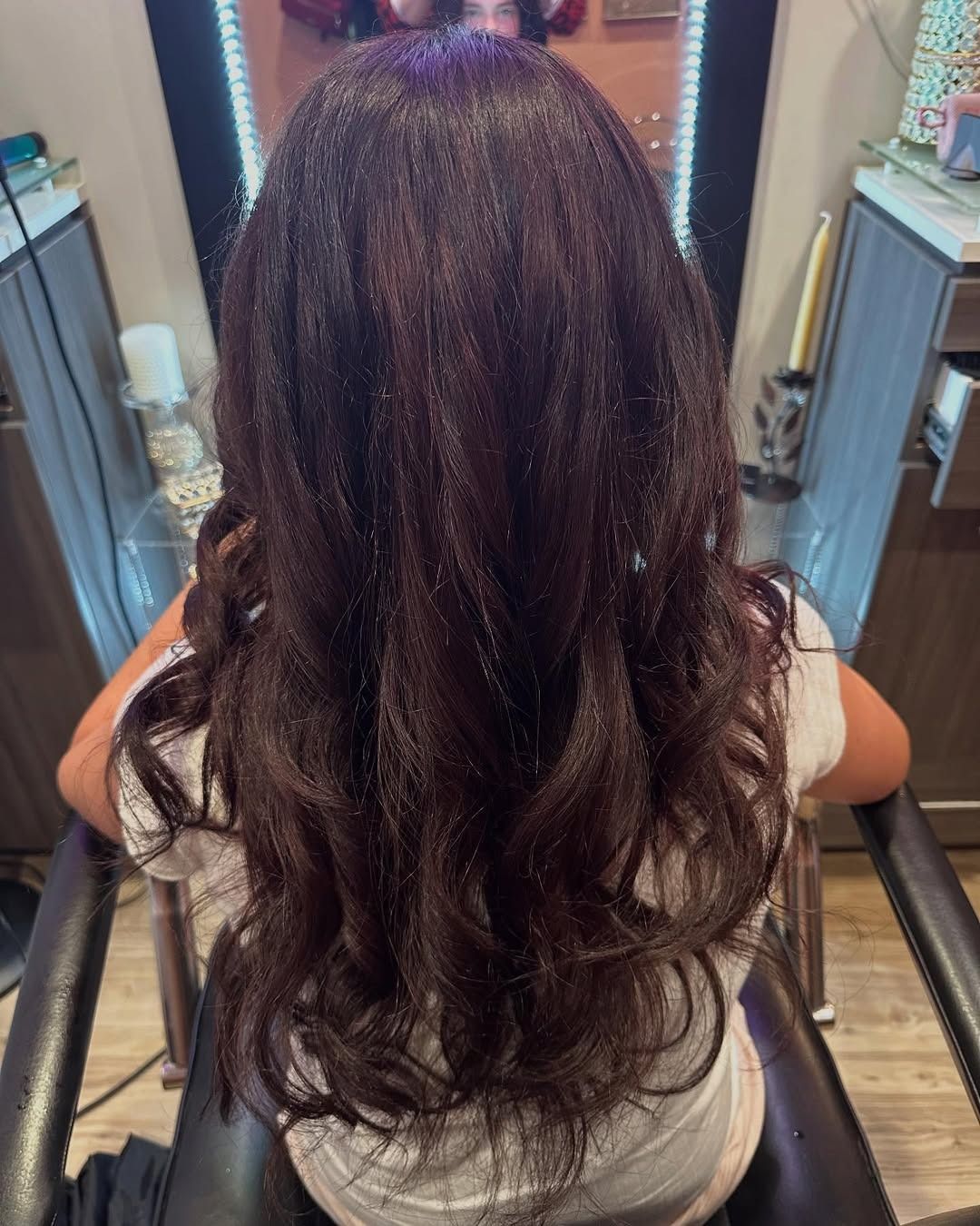 Woman with dark brown wavy hair sitting in a salon chair.